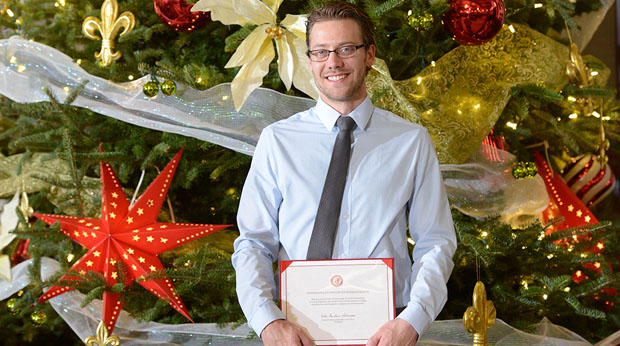 Male graduate standing in front of Christmas tree